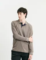 Remera de manga larga con cuello polo, confeccionada en tejido de punto canalé francés. Presenta abotonadura frontal con botones de madera y detalles a contratono en la cartera y el interior del cuello.