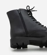 Bota de caña corta para mujer confeccionada en poliuretano (PU) color negro. Presenta punta redonda, suela tipo track con taco mediano de 3,7 cm, cordones frontales con pasadores metálicos y cierre de cremallera lateral.