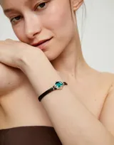 Pulsera de cuero marrón con doble tira y cristal facetado ovalado de color verde esmeralda, engarzado en metal plateado.