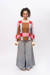 Buzo de punto con diseño geométrico de cuadros en tonos marrón, celeste, rosa y rojo. Presenta cuello redondo, puños y ruedo en color crema, con mangas largas y corte recto.