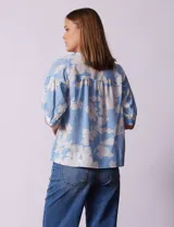 Blusa de gasa estampada con flores blancas sobre fondo celeste, marca Floral & Ivy. Cuello a la base con escote en V. Manga corta con detalle de puño y botón.