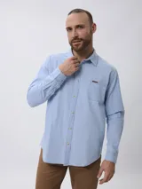 Camisa de jean manga larga en color azul claro, con cuello clásico, cierre frontal con botones y un bolsillo en el pecho con detalle de etiqueta.