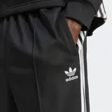 Pantalón de jogging negro Adidas Adicolor Firebird de corte holgado, con tres tiras blancas verticales a lo largo de cada pierna.