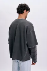 Sudadera gris oscuro de doble manga con efecto desgastado, cuello redondo y bordado frontal pequeño con texto.