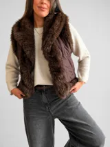 Chaleco acolchado color marrón con diseño matelassé y amplias solapas de piel sintética en tono chocolate. Presenta un corte recto y sin mangas, ideal para superposiciones.