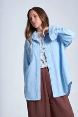 Sobrecamisa color beige confeccionada en gabardina, de corte holgado, con cuello camisero, cierre frontal con botones, dos bolsillos de parche en el pecho y mangas largas con puños abotonados.