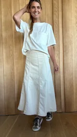 Pollera midi de denim color crudo, con corte evasé y costuras verticales decorativas que le dan estructura. Presenta un diseño de tiro medio con cierre y botón oculto.