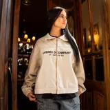 Chaqueta oversize de jean color hueso, con cuello clásico, cierre frontal de cremallera metálica, bolsillos ribeteados y estampado en el pecho.