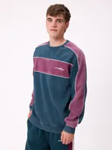 Sweater de cuello redondo marca Rusty, con diseño de bloques de color en azul marino y verde, con detalles de líneas blancas. Presenta el logo de la marca bordado en el pecho.