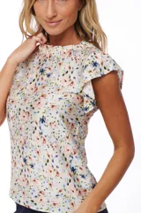 Blusa estampada con flores en tonos rosa, azul y verde sobre fondo blanco. Tiene cuello redondo y mangas cortas con volados.