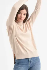 Polera tejida de cuello alto, color beige melange, de manga larga y corte holgado con aberturas laterales en el dobladillo.