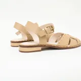 Sandalias planas de cuero color vainilla con tiras cruzadas, tachas metalizadas decorativas y tira con hebilla ajustable al tobillo.
