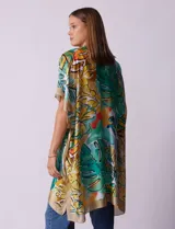 Kimono de satén con estampado tropical y hojas en tonos verdes, amarillos y naranjas sobre fondo claro. Tiene mangas anchas y corte abierto.
