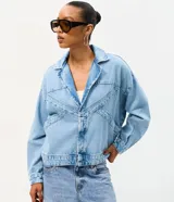 Campera de jean oversized de corte amplio con recortes estructurales, cierre frontal con botones metálicos, cuello clásico y bolsillos frontales.