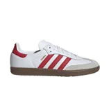 Championes Adidas modelo Samba, de diseño clásico con base de cuero blanco, franjas laterales rojas, puntera de gamuza gris y suela de goma color caramelo.