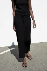 Falda midi de tiro medio en color negro, confeccionada en tejido de punto con textura y cintura elástica ajustable con cordones.