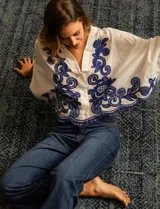 Blusa blanca de algodón con bordados azules, escote en V, cierre frontal con botones y mangas 3/4 dolman.