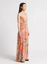 Vestido largo con estampado caleidoscópico en tonos rosa, rojo y verde. Presenta tirantes finos, escote en V, corte imperio y falda con volantes. Incluye detalle de trenzas en el pecho y la cintura que se anudan en la espalda descubierta.