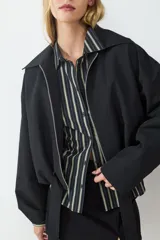 Campera corta de manga larga confeccionada en tejido técnico color negro. Presenta cuello solapa, cierre frontal con cremallera metálica y cinturón integrado con hebilla en la cintura.