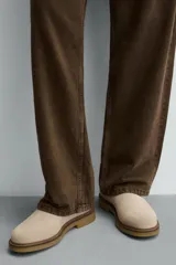 Bota estilo Chelsea de hombre, confeccionada en piel con acabado de serraje en color beige. Presenta elásticos laterales al tono, horma redonda y suela de goma a contraste con ligero tacón.