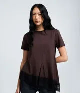 Remera de algodón color marrón chocolate, con cuello redondo, mangas cortas y corte acampanado. Presenta costuras verticales en el frente y un detalle de encaje negro aplicado en el ruedo asimétrico.