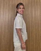Camisa de manga corta color beige, con cuello alto con volados, botonadura frontal y mangas abullonadas con terminación fruncida.