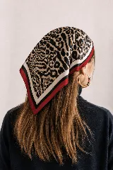 Pañuelo cuadrado de satén con estampado de leopardo y detalles de franjas en color rojo, blanco y negro en los bordes.