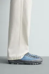 Zapatilla de cordones con diseño de inspiración montañista, confeccionada en piel con acabado de serraje en color azul. Presenta una puntera y refuerzo lateral en gamuza gris con textura desgastada, horma redonda y suela de goma dentada VIBRAM®.