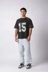 Remera de algodón con efecto de lavado gastado, corte holgado y diseño deportivo. Presenta el número 15 estampado en el frente con acabado desgastado y detalles de costuras blancas en los hombros y laterales.