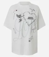 Remera de corte boxy en algodón color blanco, con cuello redondo y mangas cortas. Presenta un estampado frontal con diseño de cupido, un corazón formado por una cadena, la frase 'Cupid's Favorite' y detalles de alfileres de gancho dispersos.