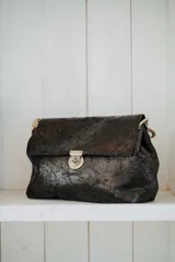 Cartera de hombro con textura efecto cocodrilo en color marrón oscuro. Presenta un diseño rectangular con solapa frontal, cierre metálico a presión y una correa de cadena gruesa en tono dorado.