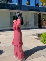 Vestido largo de fiesta color rosa viejo, con cuello alto, mangas largas con volados en los puños y falda con volados escalonados. Presenta una cintura elástica fruncida que define la silueta.