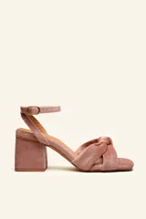Sandalia de tacón cuadrado medio, confeccionada en terciopelo color rosado. Presenta un diseño con tiras cruzadas y anudadas en la parte frontal, y una tira ajustable con hebilla metálica en el tobillo.