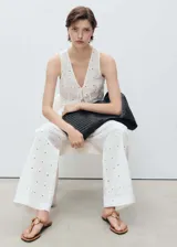 Pantalon de tiro medio con diseño recto y largo, confeccionado en tejido de algodón con bordado floral y detalles calados. Cuenta con cierre delantero de botón, gancho y cremallera ocultos, trabillas y bolsillos laterales.