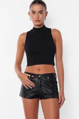 Short negro de cuerina, tiro medio, con bolsillos delanteros y traseros, presillas en la cintura y cierre con botón metálico y cremallera.