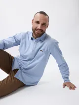 Camisa de jean manga larga en color azul claro, con cuello clásico, cierre frontal con botones y un bolsillo en el pecho con detalle de etiqueta.