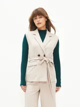 Chaleco beige con solapas, doble botonadura, lazo para atar en la cintura y bolsillos delanteros.