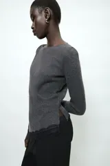 Top de manga larga en tejido de punto suave color gris, con cuello redondo y bajo asimétrico decorado con encaje negro a tono. Presenta detalles de encaje negro en los puños.