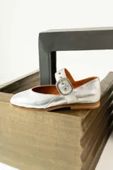 Zapatos tipo Mary Jane de charol negro con punta cuadrada y tira con hebilla metálica dorada sobre el empeine. Interior forrado en cuero color suela.