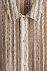 Camisa de manga corta con cuello inglés y botones frontales, confeccionada en tejido de punto pointelle con patrón de rayas verticales en tonos tierra y beige.