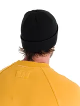 Gorro tipo beanie de punto acanalado en color negro, con puño enrollado y etiqueta de marca Caterpillar en el frente.