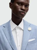 Blazer de hombre color azul claro con textura de tejido tipo lino o mezcla, de corte estructurado con solapas de muesca, dos botones frontales blancos y bolsillos de parche.