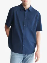 Camisa azul marino de manga corta, con cuello clásico, cierre frontal con botones, bolsillo de parche en el pecho izquierdo y logo CK bordado en el bolsillo.