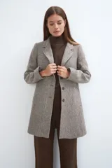 Saco corto entallado de lana fina, con cuello solapa, manga larga y cierre frontal con botones. Presenta un diseño clásico con textura de espiga en tonos tierra.