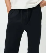Pantalón jogger de sarga color negro, con cintura elástica con cordón de ajuste, bolsillos laterales y traseros, y puños elásticos en los tobillos.