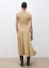 Vestido midi de corte evasé en color beige, con cuello en pico y manga corta. Presenta un diseño con costuras verticales decorativas y cierre de cremallera en la parte posterior.