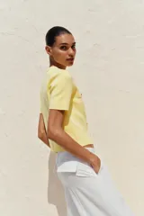 Chaqueta de punto color amarillo pálido, con cuello redondo, manga corta, cierre frontal con botones dorados y bolsillos de parche en el pecho.