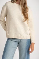 Sweater de lana color crema con motas multicolores, de corte oversize, cuello redondo y mangas largas. Presenta un diseño con costuras decorativas frontales y terminaciones en tejido acanalado.