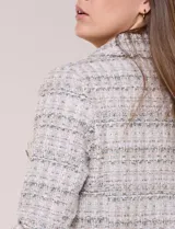 Chaqueta confeccionada en tejido de tweed beige con trama estructurada. Presenta cuello con solapa, frente abierto con botones metálicos y cuatro bolsillos funcionales. Las mangas largas de calce recto cuentan con bocamangas decoradas con botones y terminaciones deshilachadas al igual que los bordes.