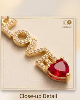 Collar de bronce dorado con cadena fina y dije vertical con la palabra 'LOVE' pavimentada en circonias brillantes y rematada con un corazón rojo en la parte inferior.